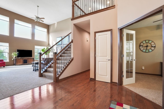 foyer featuring wood finished floors, a ceiling fan, a high ceiling, and stairway
