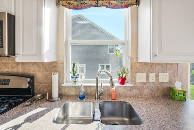 kitchen with white cabinets, gas stove, decorative backsplash, and a sink