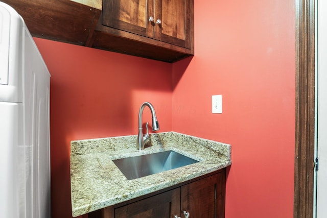 kitchen with a sink, light stone countertops, refrigerator, and dark brown cabinets