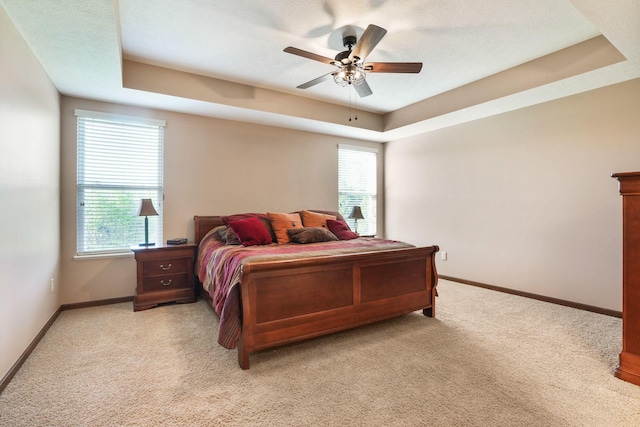 bedroom featuring a raised ceiling, multiple windows, light carpet, and baseboards