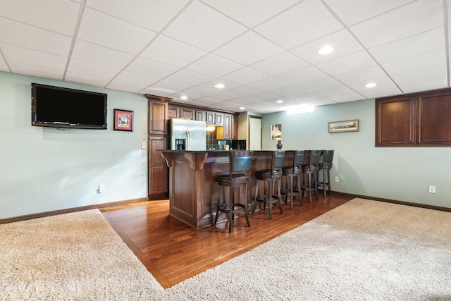 bar featuring wood finished floors, baseboards, stainless steel refrigerator with ice dispenser, recessed lighting, and wet bar