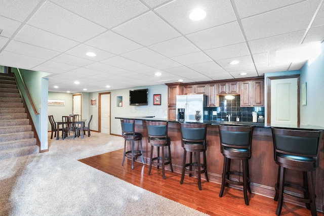 kitchen featuring wood finished floors, dark countertops, a breakfast bar area, stainless steel refrigerator with ice dispenser, and tasteful backsplash