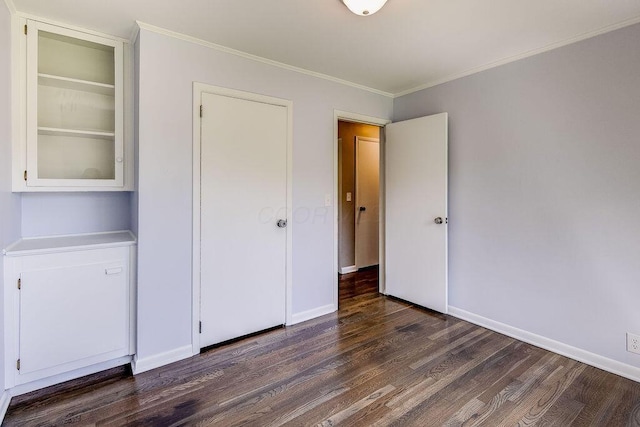 unfurnished bedroom with crown molding, dark wood-style flooring, and baseboards