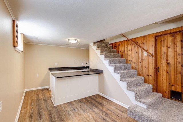 bar featuring wood finished floors, a sink, baseboards, indoor wet bar, and stairs