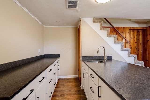 kitchen featuring visible vents, crown molding, dark wood-type flooring, white cabinets, and a sink