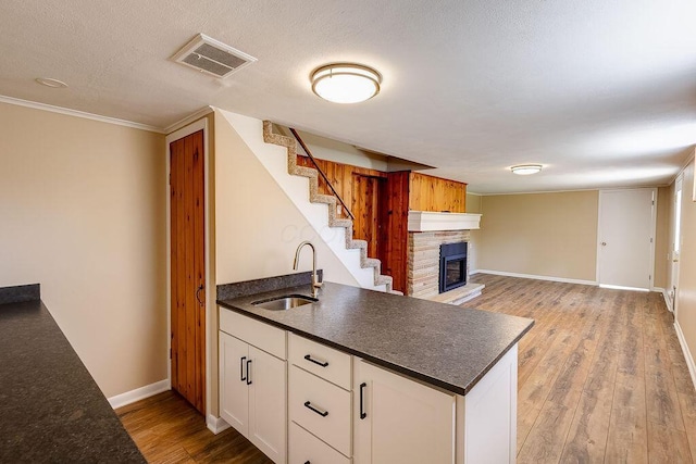 kitchen with a sink, dark countertops, a fireplace, and visible vents