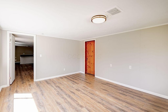 spare room with crown molding, baseboards, light wood finished floors, and visible vents