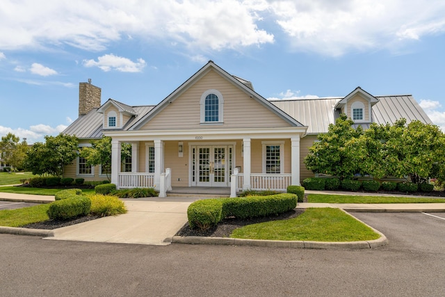 view of front of home with french doors, a chimney, a standing seam roof, metal roof, and a porch