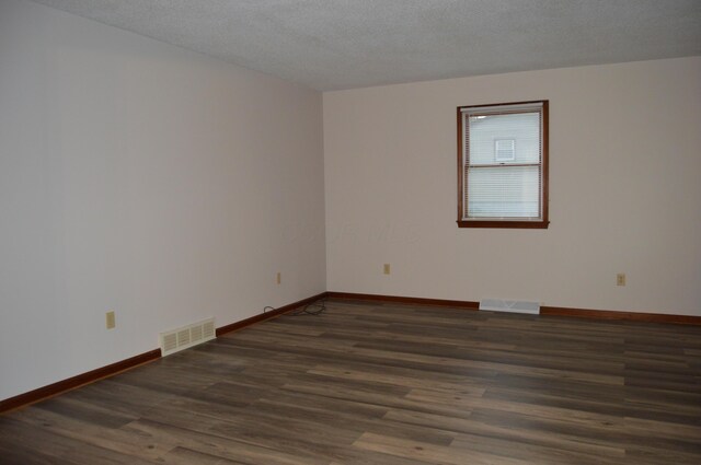spare room featuring visible vents, a textured ceiling, dark wood-style flooring, and baseboards