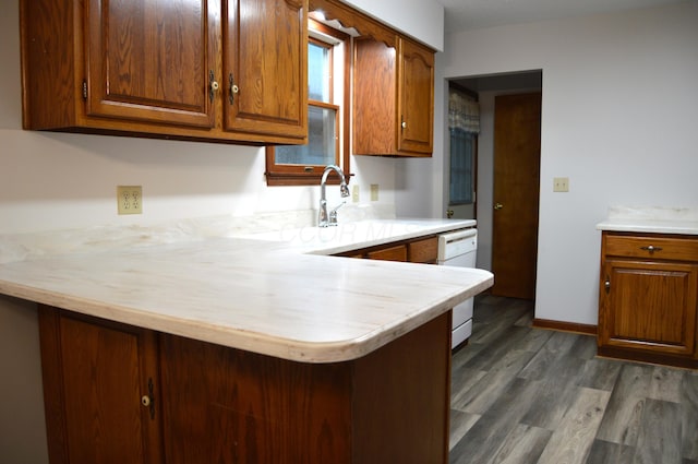 kitchen featuring brown cabinets, dark wood-style flooring, white dishwasher, light countertops, and a peninsula