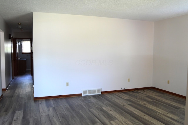 empty room featuring visible vents, a textured ceiling, baseboards, and dark wood-style floors