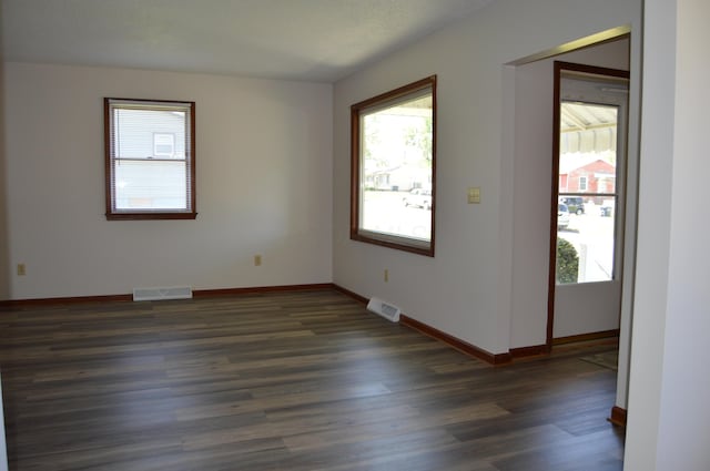 unfurnished room featuring visible vents, dark wood-style flooring, and a healthy amount of sunlight