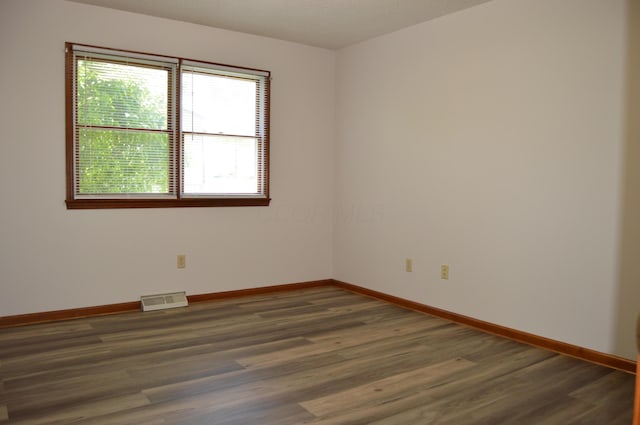 empty room featuring baseboards, wood finished floors, and visible vents