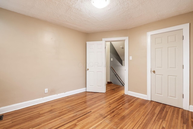 unfurnished bedroom with baseboards, light wood finished floors, a textured ceiling, and visible vents