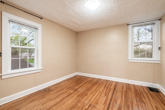 empty room featuring a textured ceiling, plenty of natural light, light wood-style flooring, baseboards, and visible vents