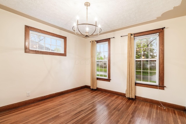 empty room with a textured ceiling, baseboards, an inviting chandelier, and hardwood / wood-style flooring