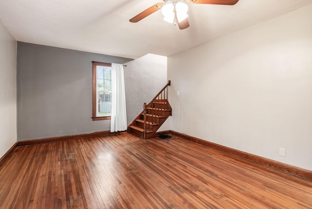 unfurnished room featuring a ceiling fan, stairway, baseboards, and hardwood / wood-style flooring