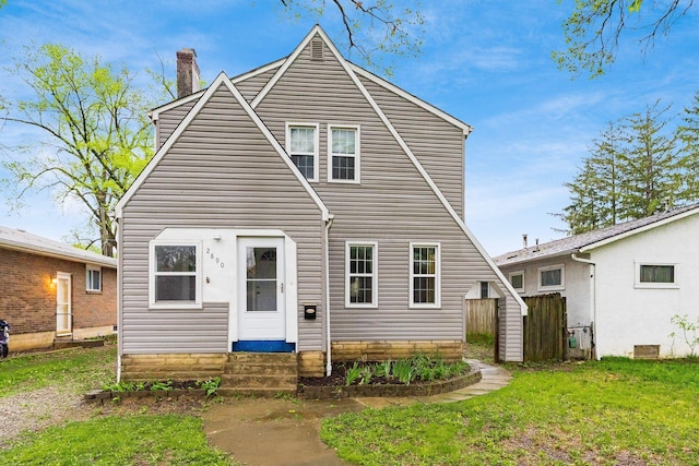 view of front of property featuring entry steps, fence, a chimney, and a front yard