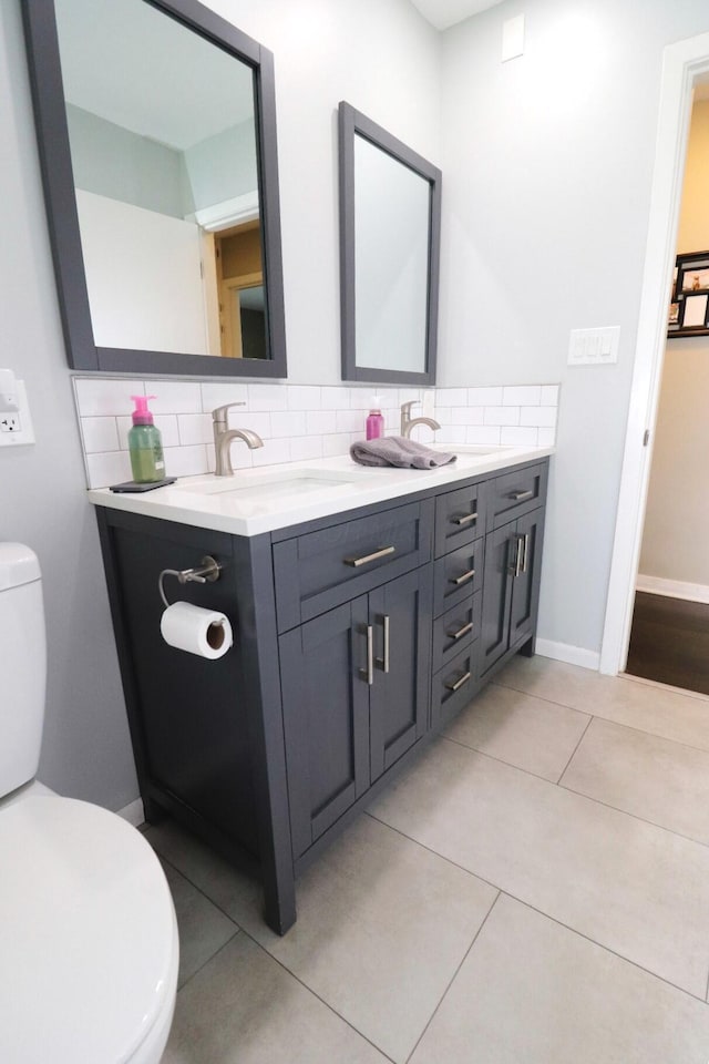 bathroom with double vanity, decorative backsplash, toilet, baseboards, and a sink