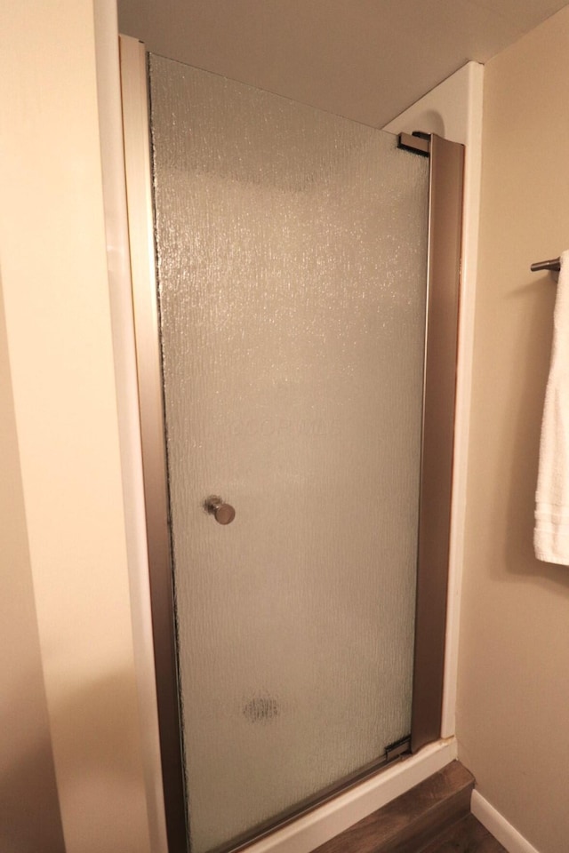 full bath with baseboards, a shower stall, and wood finished floors