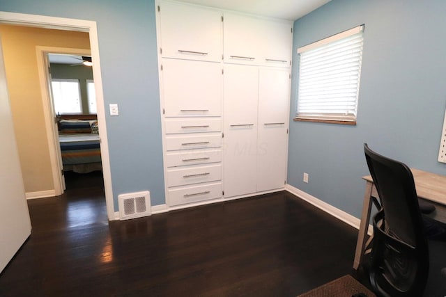 unfurnished office with baseboards, ceiling fan, dark wood-type flooring, and visible vents