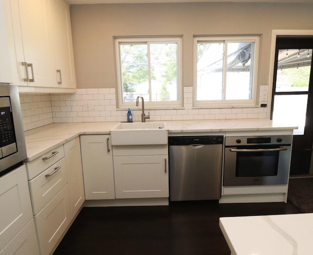 kitchen featuring appliances with stainless steel finishes, light stone counters, a sink, white cabinetry, and backsplash