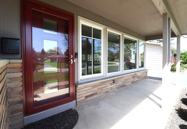 view of exterior entry featuring covered porch and brick siding