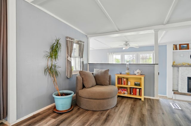 sitting room featuring visible vents, wood finished floors, beam ceiling, a fireplace, and ceiling fan
