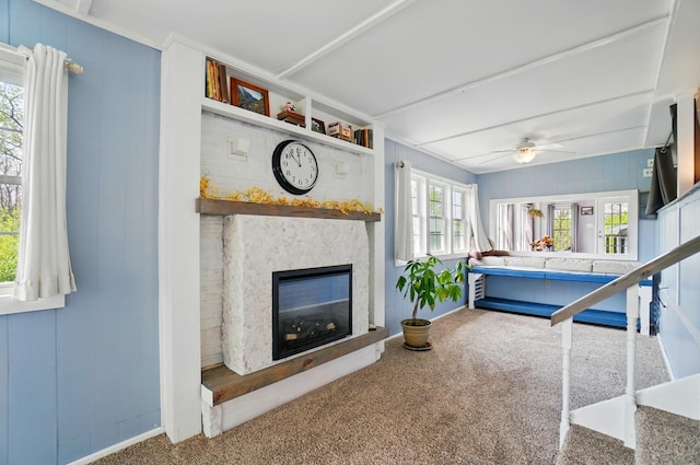 living area featuring baseboards, carpet, ceiling fan, and a glass covered fireplace