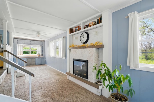 living area with a glass covered fireplace, ceiling fan, and carpet