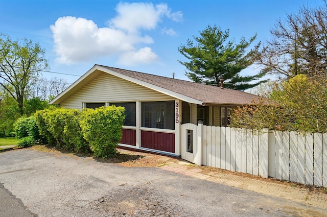 view of side of property with a sunroom, fence, and roof with shingles