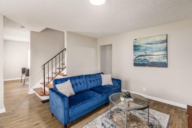 living room featuring a textured ceiling, stairs, baseboards, wood finished floors, and visible vents