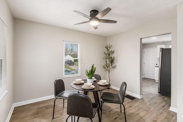 dining room with baseboards, light wood finished floors, ceiling fan, and visible vents