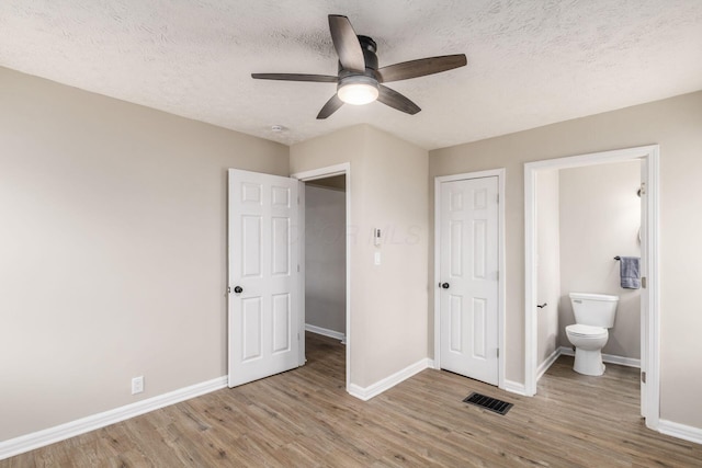 unfurnished bedroom featuring visible vents, wood finished floors, baseboards, ensuite bathroom, and a textured ceiling