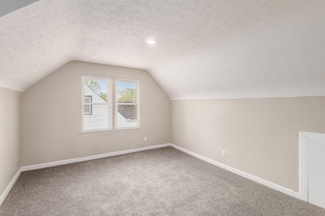additional living space with a textured ceiling, vaulted ceiling, baseboards, and carpet
