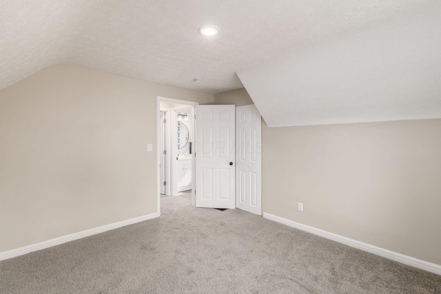 additional living space with baseboards, vaulted ceiling, a textured ceiling, and light colored carpet