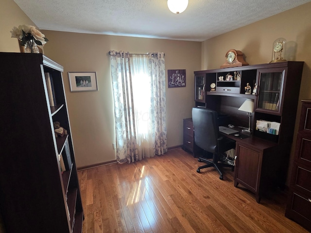 home office featuring light wood finished floors, a textured ceiling, and baseboards