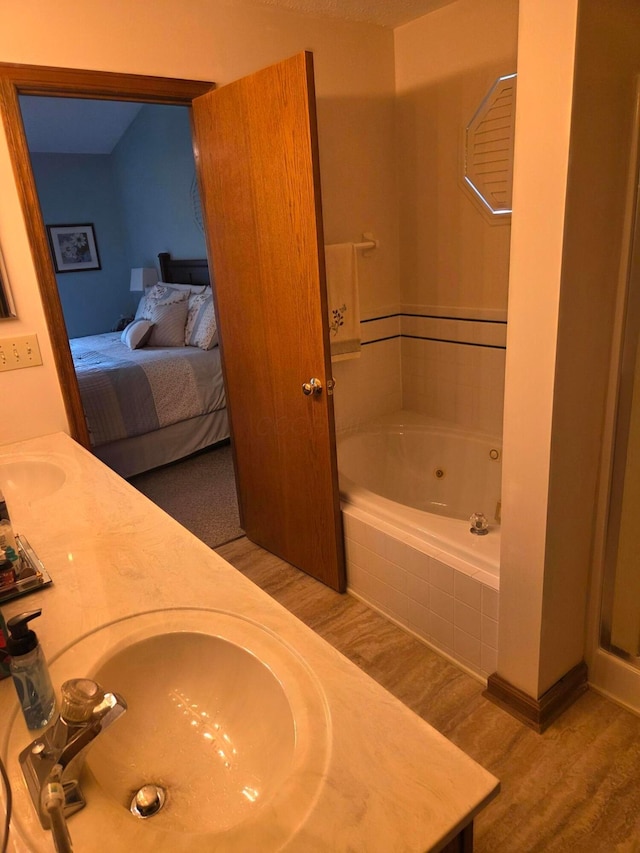 ensuite bathroom featuring a sink, connected bathroom, double vanity, wood finished floors, and a tub with jets