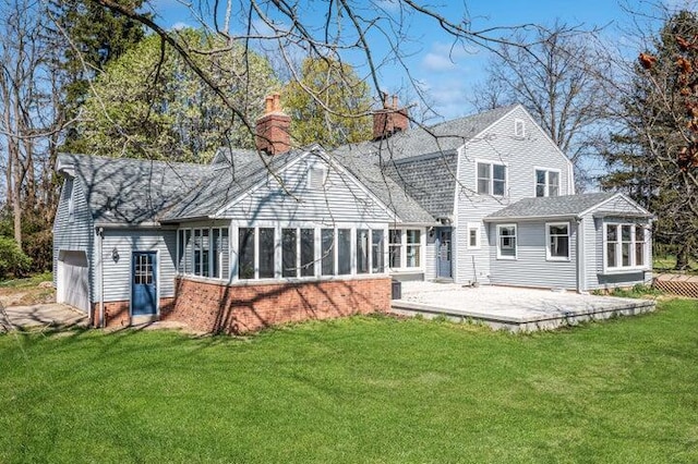 back of property featuring a garage, a sunroom, a chimney, a patio area, and a yard