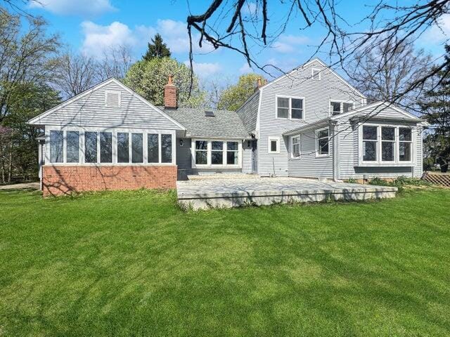 rear view of house with a lawn, brick siding, a chimney, and a patio area