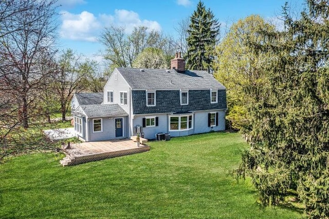 rear view of property with roof with shingles, central air condition unit, a gambrel roof, a deck, and a lawn