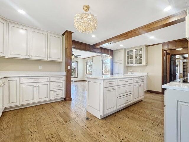 kitchen with beam ceiling, glass insert cabinets, light countertops, white cabinets, and light wood-style flooring