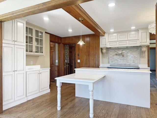 kitchen with glass insert cabinets, light countertops, tasteful backsplash, light wood finished floors, and hanging light fixtures