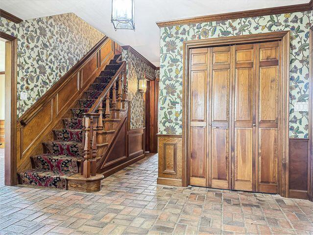 staircase featuring crown molding, brick floor, and wallpapered walls