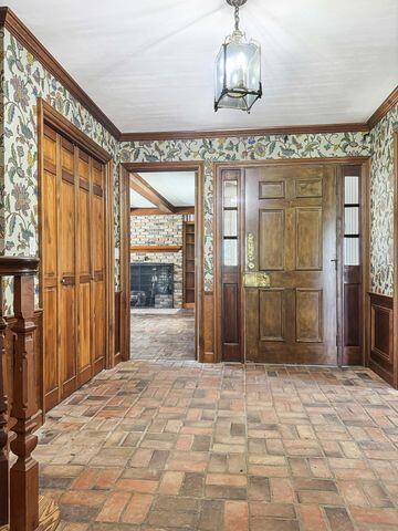 foyer entrance with wallpapered walls, wainscoting, brick floor, and a fireplace