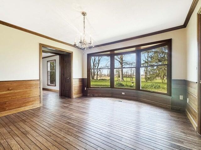 unfurnished dining area with an inviting chandelier, crown molding, a healthy amount of sunlight, and hardwood / wood-style floors