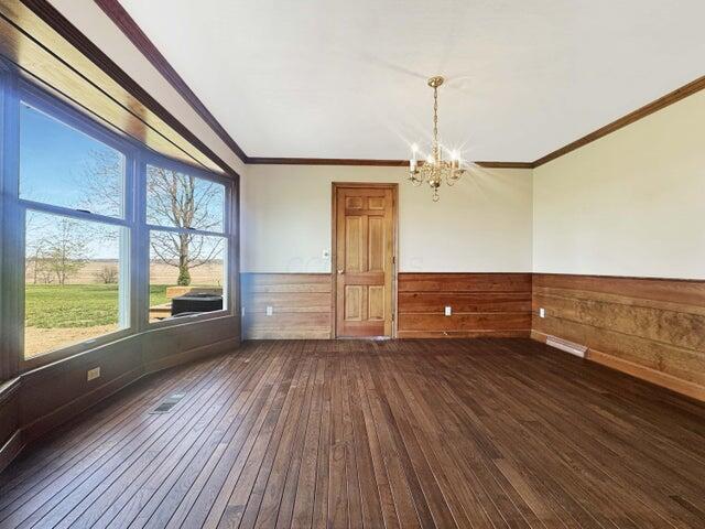 empty room featuring a chandelier, dark wood-style floors, ornamental molding, and a wainscoted wall