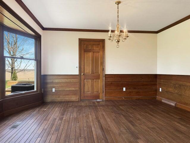 unfurnished room featuring ornamental molding, wood walls, a wainscoted wall, a chandelier, and hardwood / wood-style flooring