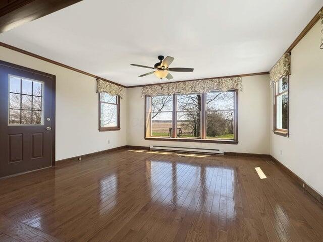 interior space with crown molding, ceiling fan, hardwood / wood-style floors, baseboards, and a baseboard heating unit