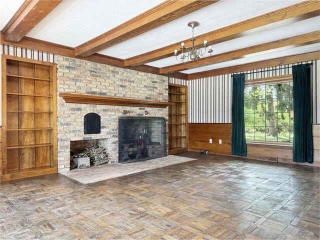 unfurnished living room with built in features, a fireplace, beam ceiling, a chandelier, and wooden walls